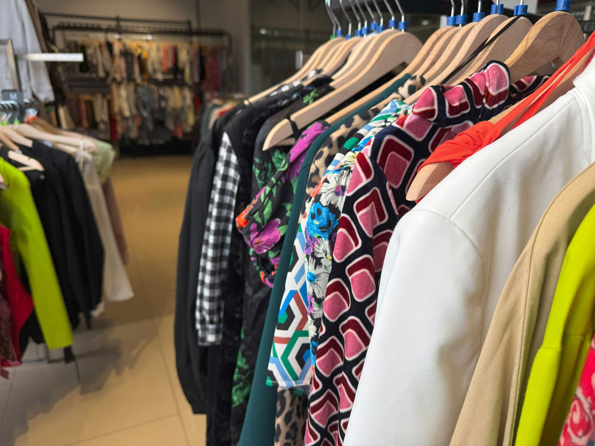 A vibrant clothing rack displays a colorful variety of dresses, jackets, and patterned outfits